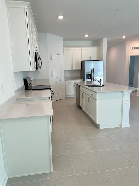 A modern kitchen features white cabinetry, stainless steel appliances, a center island, and tiled floors — 2981 GOOD VIBES WAY, CLERMONT, FL