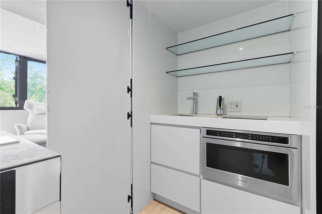 A modern kitchenette features white cabinetry, a built-in microwave, glass shelving, and a sink — 63 KINGS CT UNIT #3A, SAN JUAN, PR