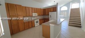A kitchen with wood cabinets, a white refrigerator, and a staircase leading to an upper level — 13161 SW 45th Dr, Miramar FL 33027, MIRAMAR, FL