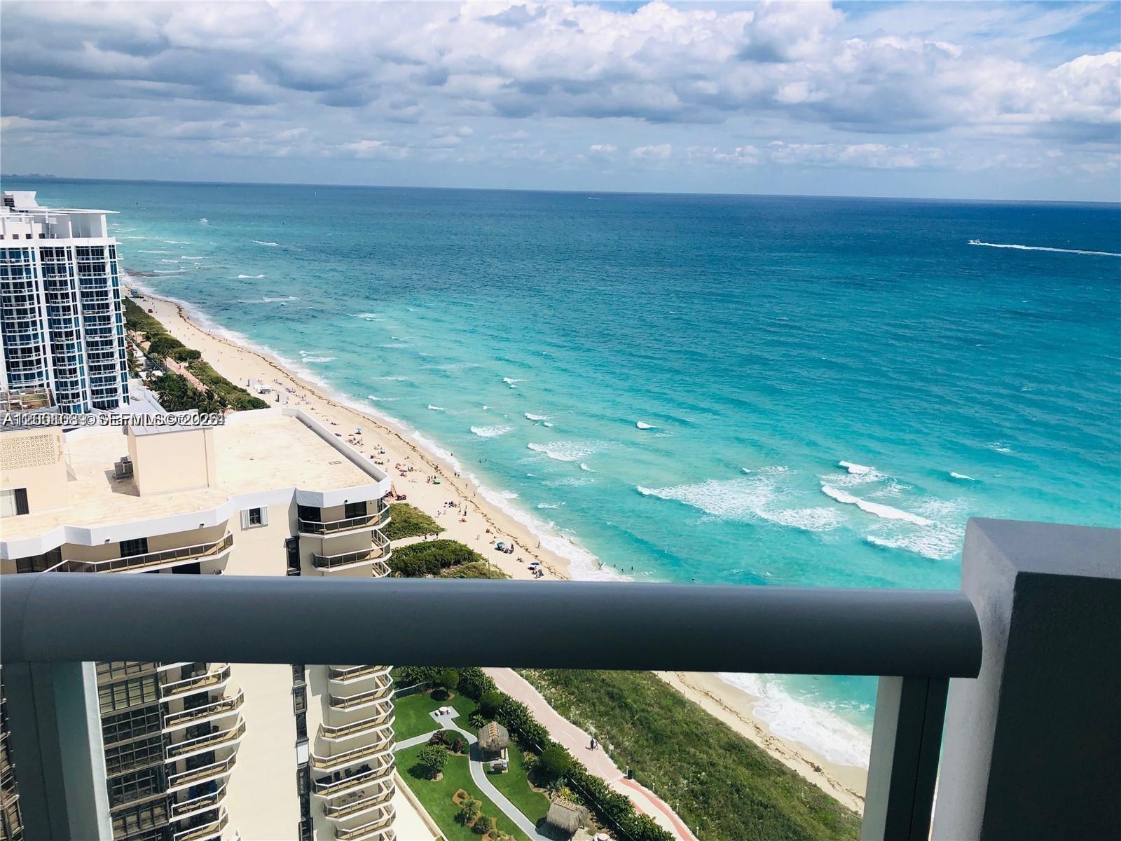 A high-angle view from a balcony overlooks a sandy beach and the turquoise ocean — 6365 Collins Ave # 2710, Miami Beach FL 33141, MIAMI BEACH, FL