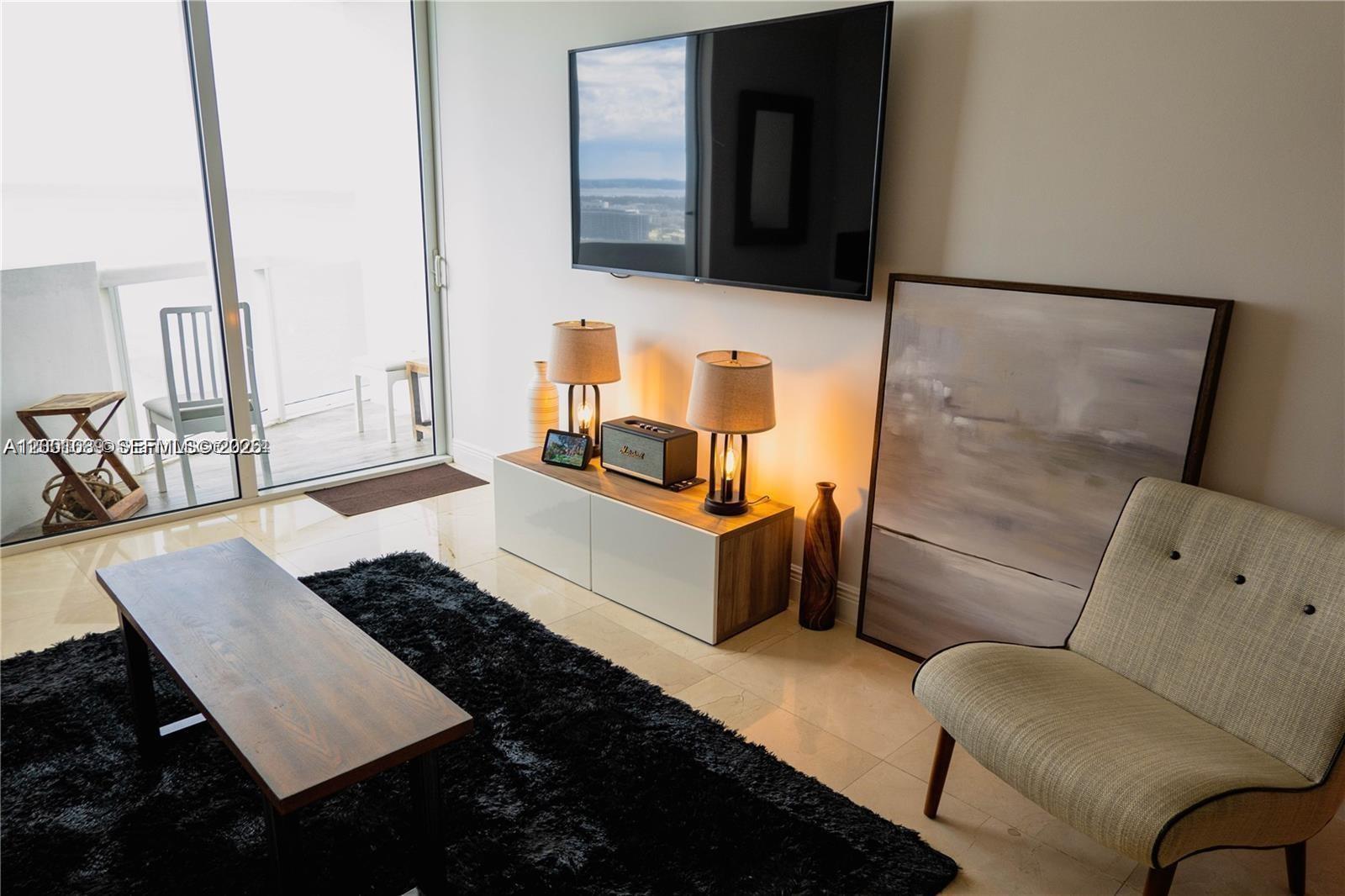 A living room features a television, media console, black rug, and a beige armchair — 6365 Collins Ave # 2710, Miami Beach FL 33141, MIAMI BEACH, FL