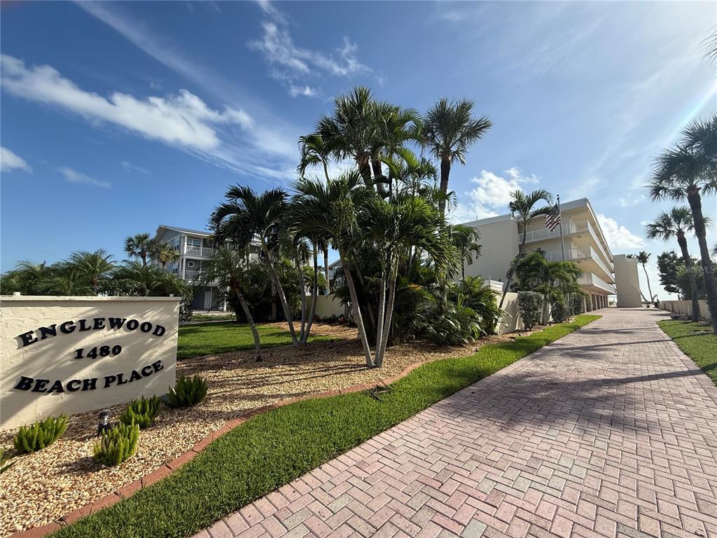 A paved walkway leads past a sign and palm trees toward a multi-story apartment building — 1480 GULF BOULEVARD UNIT 304, ENGLEWOOD, FL