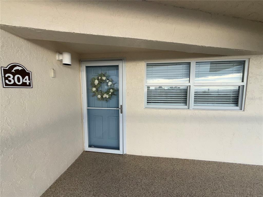The exterior view shows a light-colored building entrance with a numbered sign and window — 1480 GULF BOULEVARD UNIT 304, ENGLEWOOD, FL
