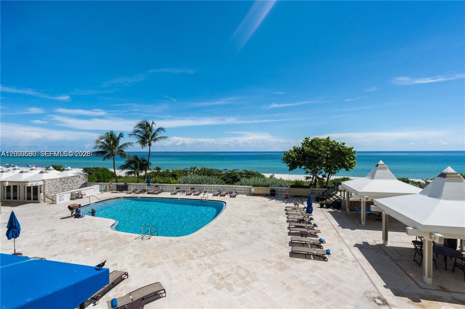 An outdoor swimming pool area features lounge chairs, cabanas, and a view of the ocean — 5555 Collins ave # 9V, Miami Beach FL 33140, MIAMI BEACH, FL