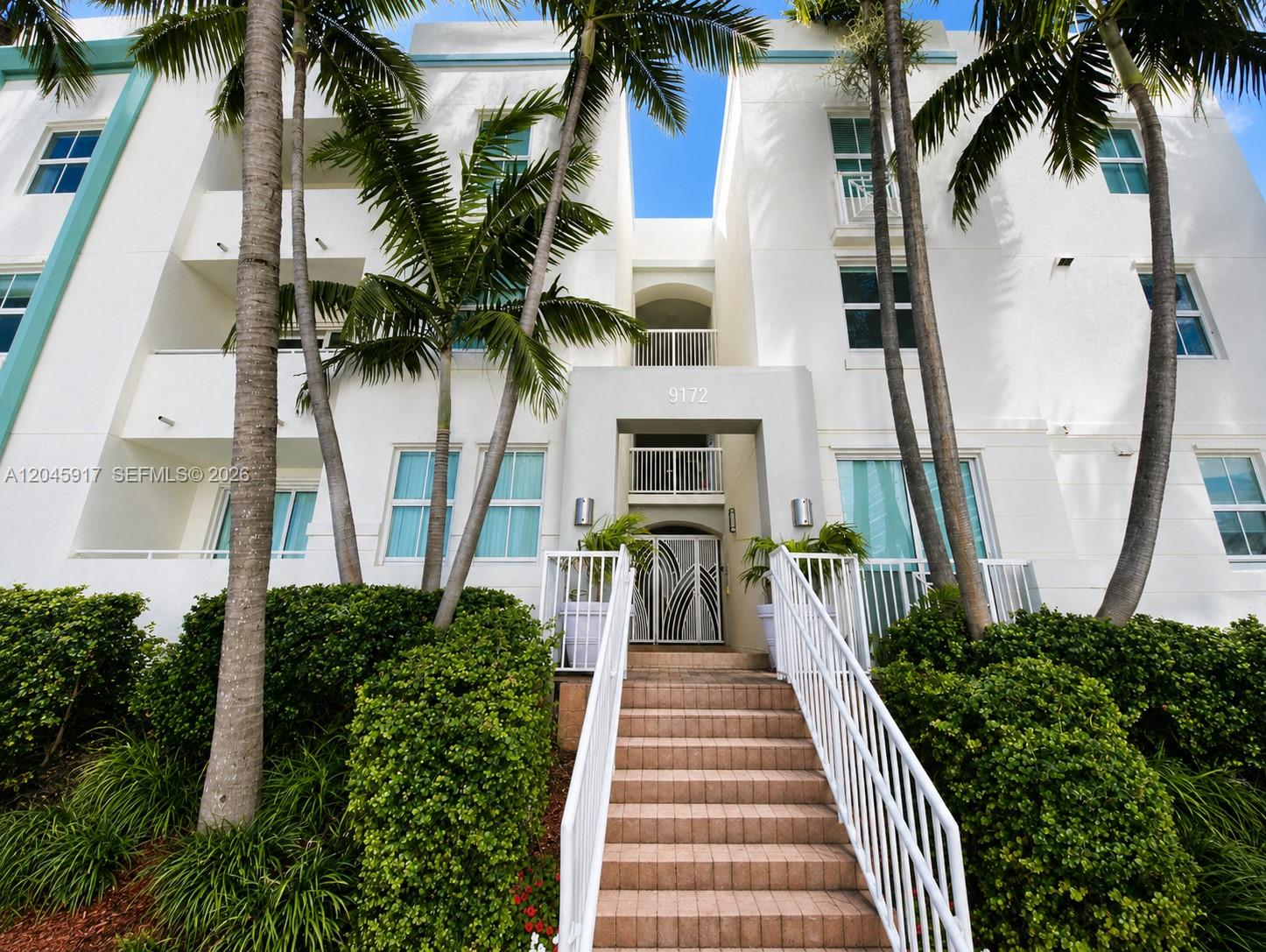 A white multi-story building entrance features a central staircase leading to a gated doorway — 9172 Collins Ave # 218, Surfside FL 33154, SURFSIDE, FL