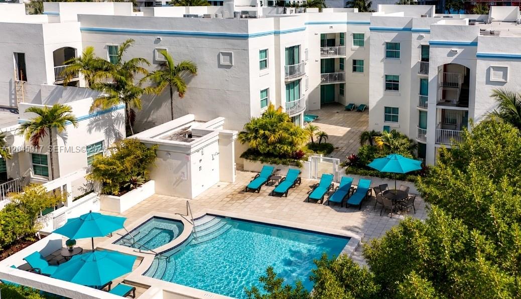 An aerial view shows a swimming pool with lounge chairs and a multi-story apartment building — 9172 Collins Ave # 218, Surfside FL 33154, SURFSIDE, FL