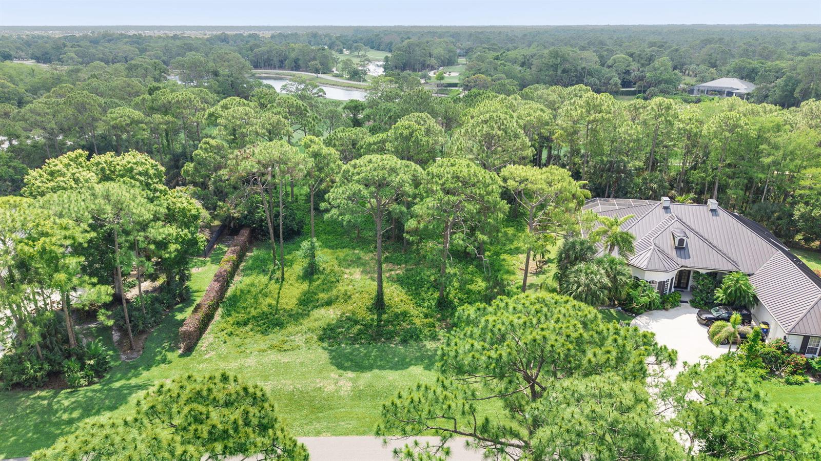 An aerial view of a residential lot with a house, driveway, and surrounding wooded area — 19051 SE Old Trail Drive W, Jupiter FL 33478, JUPITER, FL