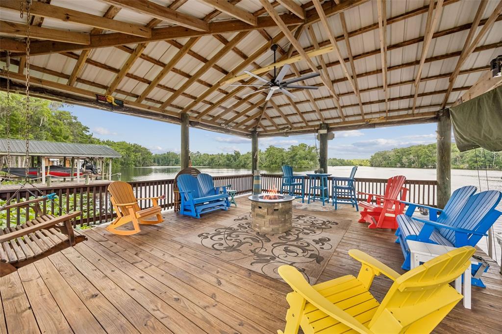 A covered wooden deck overlooking a river features a fire pit and colorful outdoor furniture — 329 PARADISE CIRCLE, SATSUMA, FL