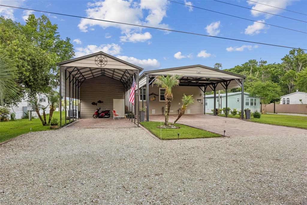 A house exterior features two attached carports over a paved driveway and a gravel front yard — 329 PARADISE CIRCLE, SATSUMA, FL