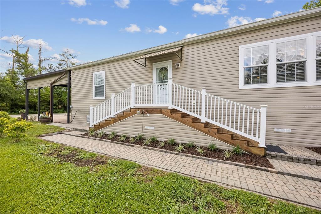 A tan mobile home features a white front door with stairs and a paved walkway — 329 PARADISE CIRCLE, SATSUMA, FL
