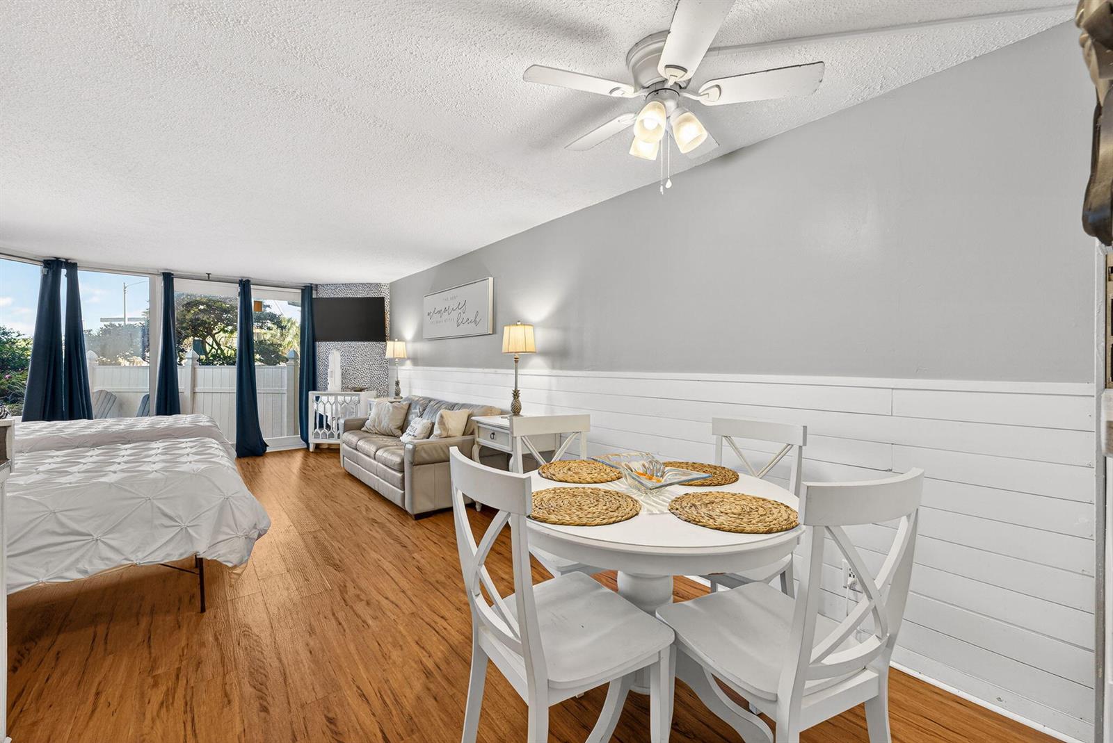 A studio room features a dining set, a sofa, and a bed near a patio door — 8817 S Thomas Drive # A114, Panama City FL 32408, PANAMA CITY, FL