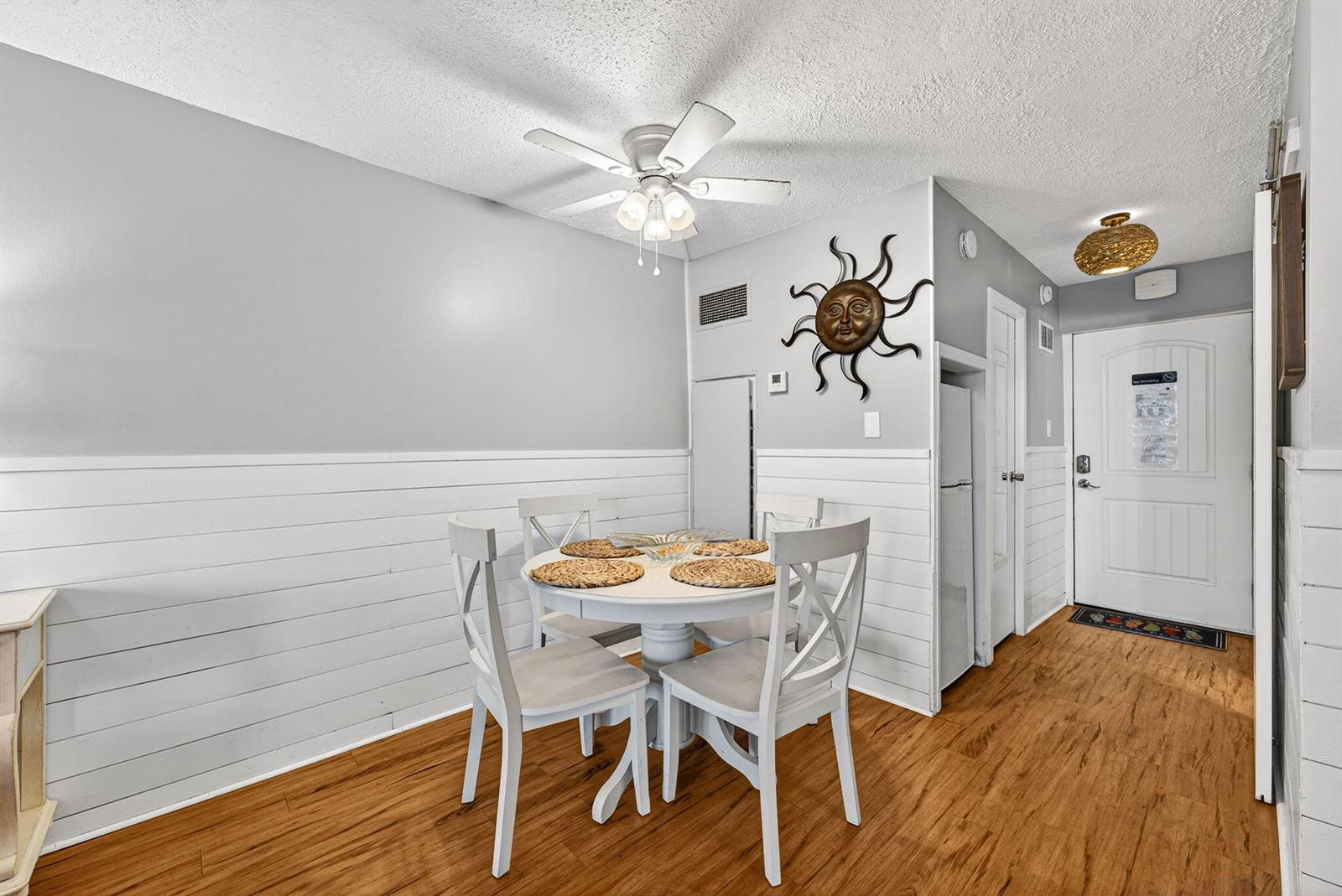 A dining area features a white round table, four chairs, shiplap walls, and wood flooring — 8817 S Thomas Drive # A114, Panama City FL 32408, PANAMA CITY, FL