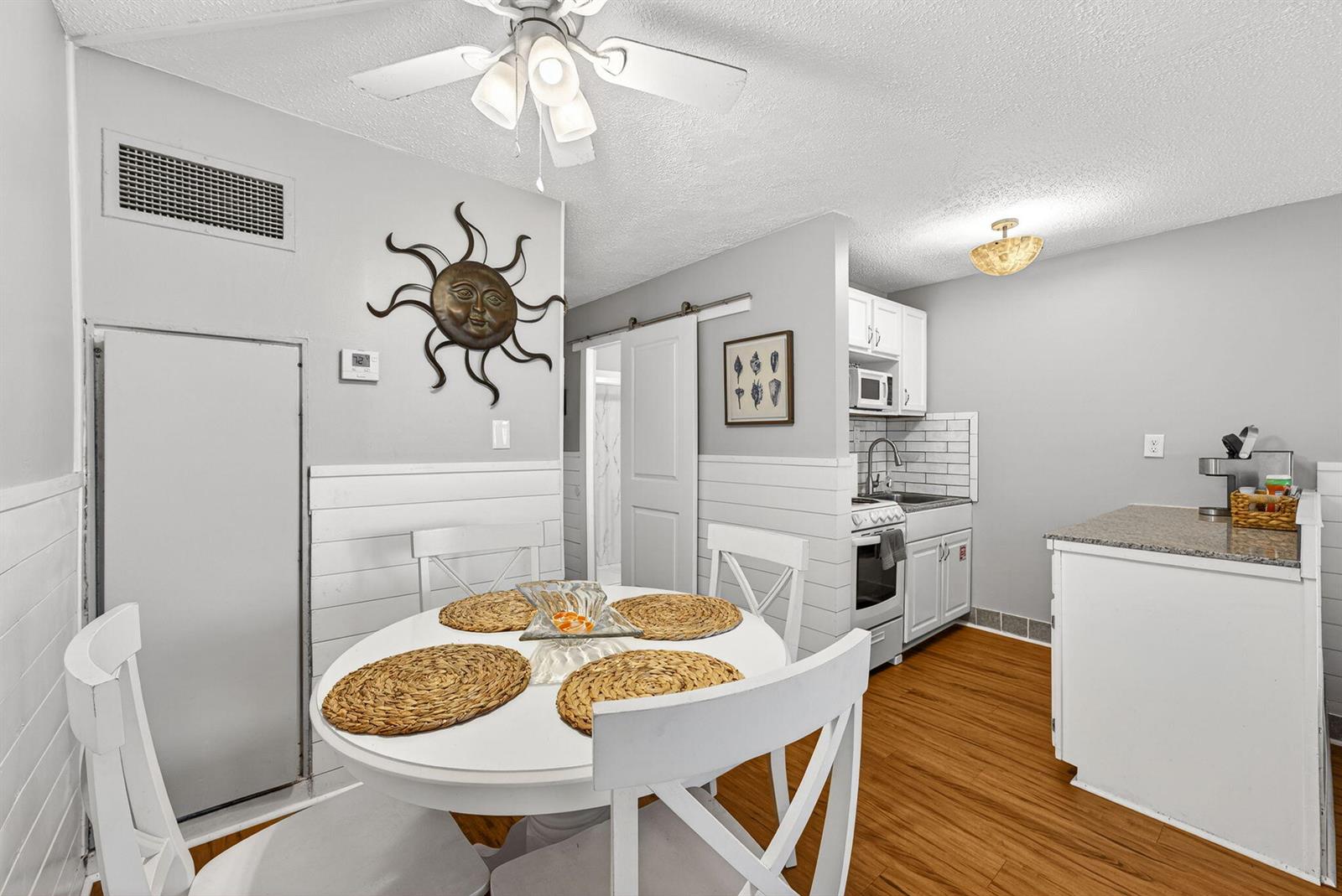 A dining area with a round white table and chairs sits adjacent to a small kitchen — 8817 S Thomas Drive # A114, Panama City FL 32408, PANAMA CITY, FL