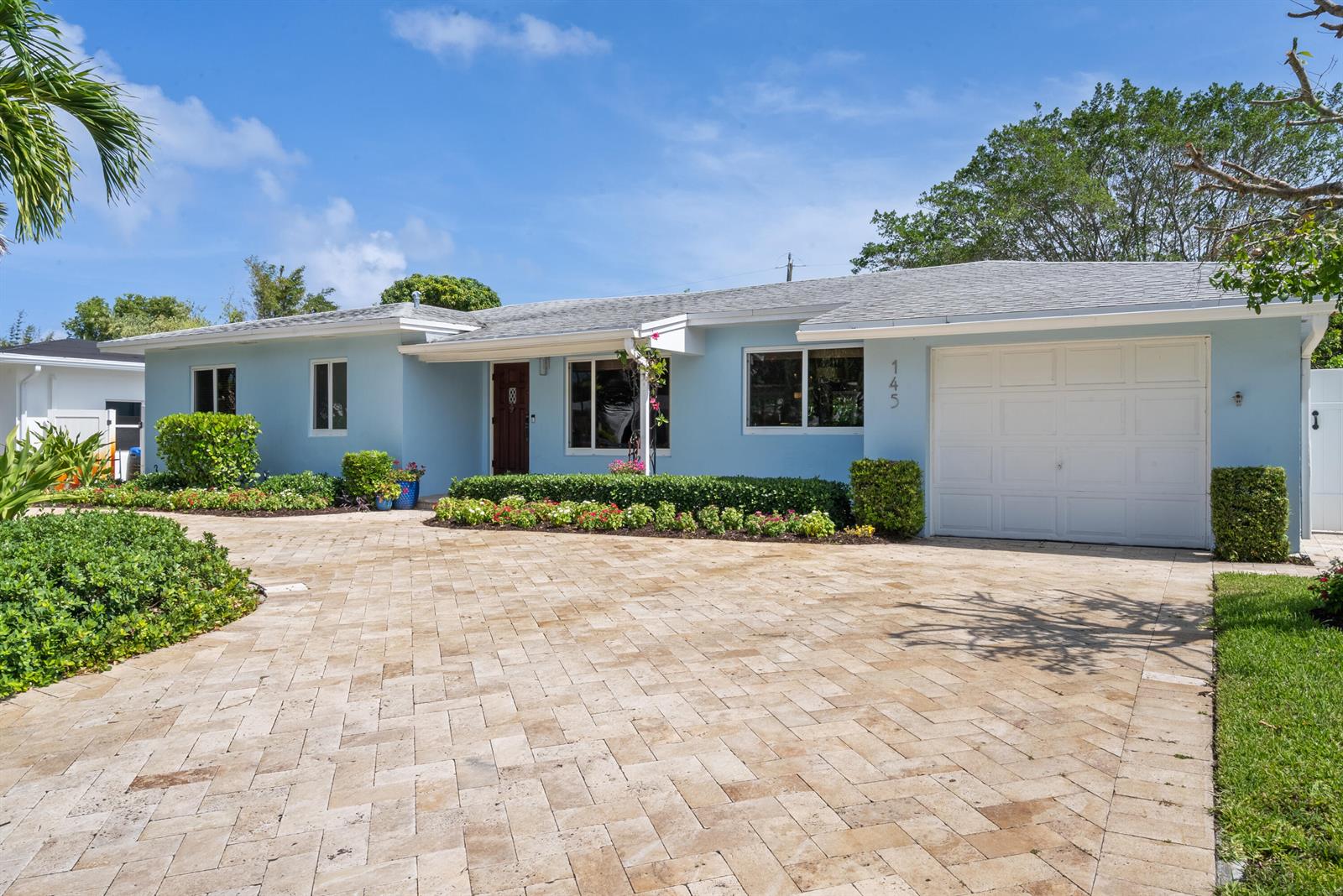 A light blue single-story house features a paved driveway, a garage, and landscaped garden beds — 145 Vassar Drive, FL 33460, FL