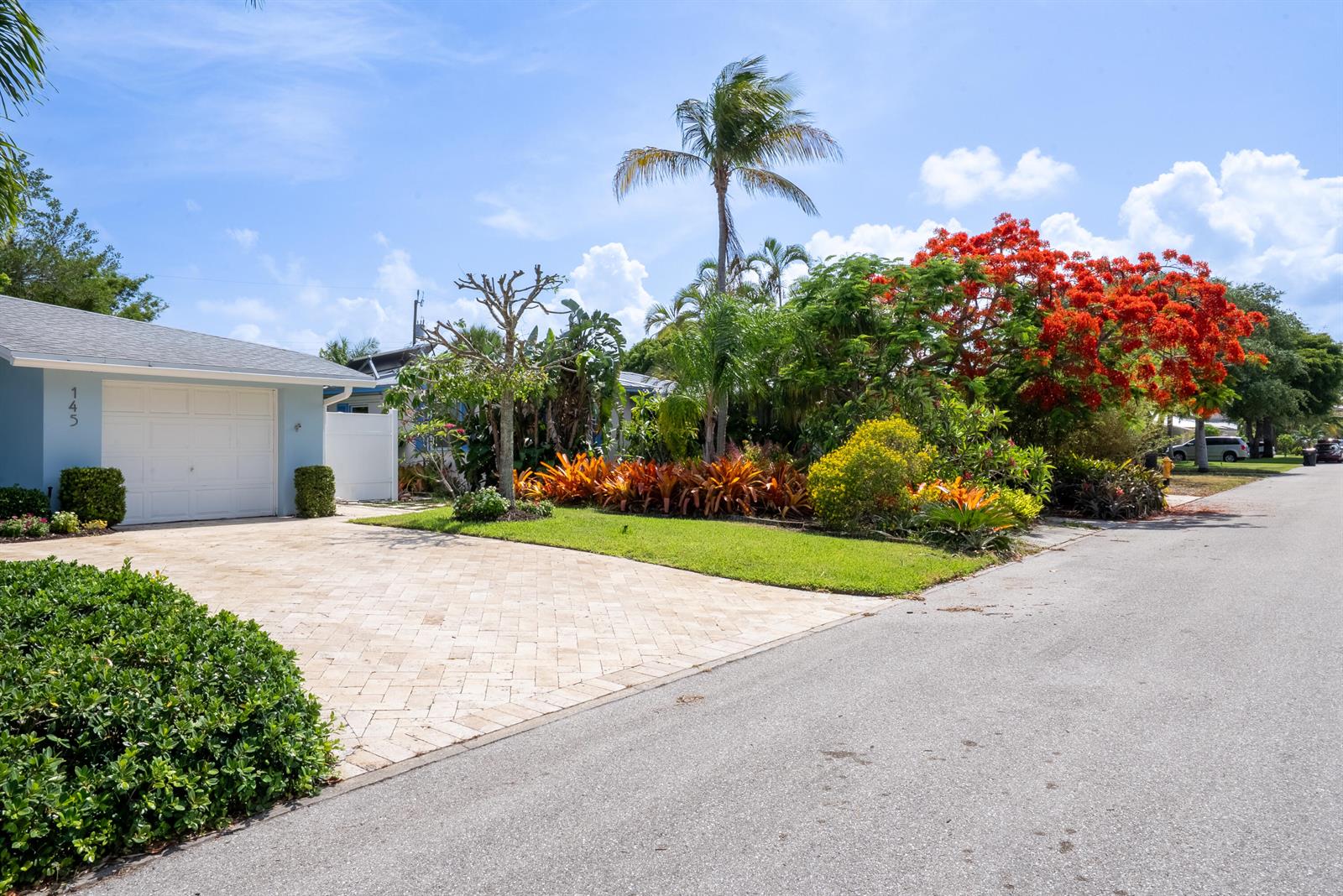 A light blue house with a paved driveway and vibrant tropical landscaping under a blue sky — 145 Vassar Drive, FL 33460, FL
