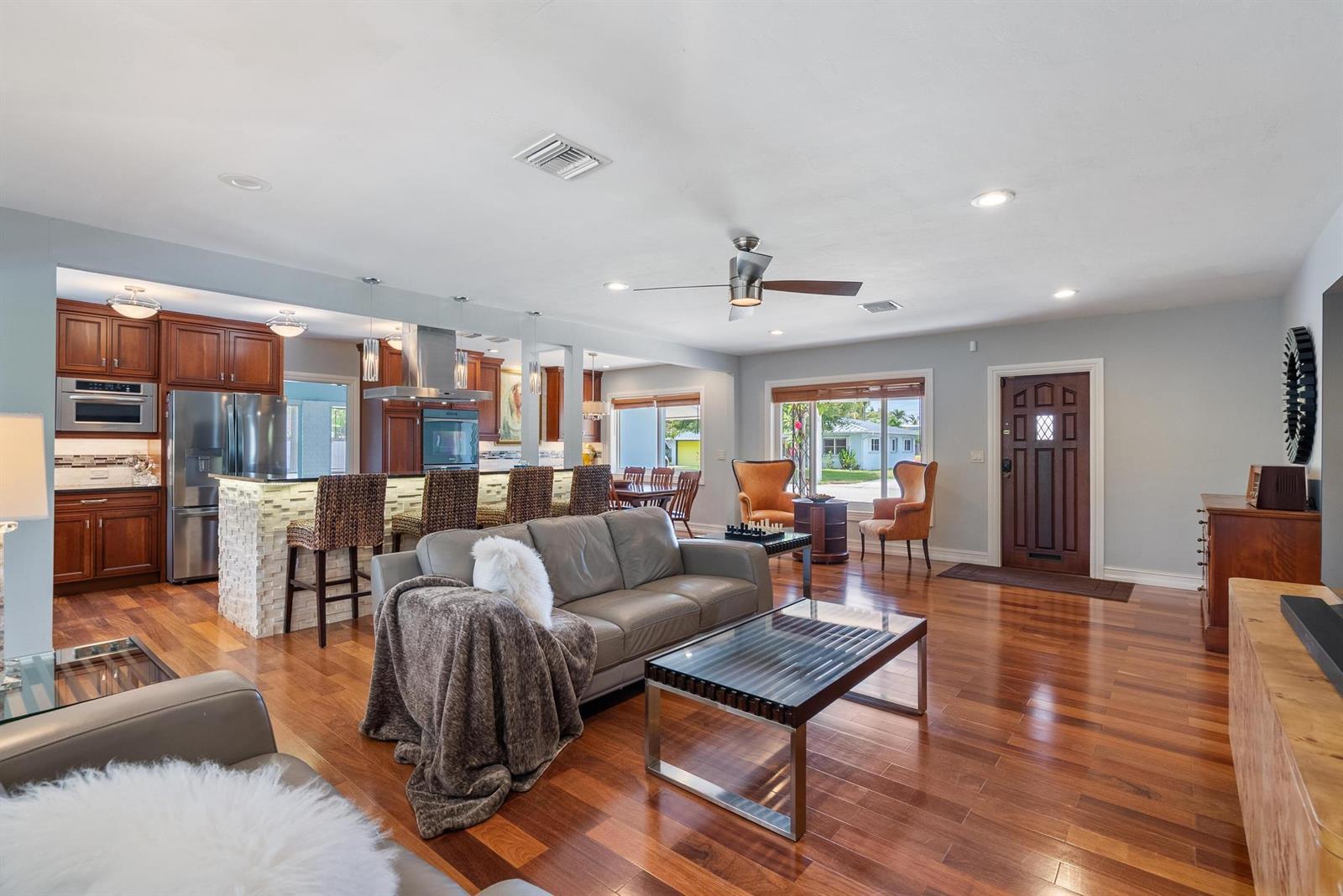 An open-concept living room and kitchen featuring hardwood floors, a stone-faced island, and leather seating — 145 Vassar Drive, FL 33460, FL