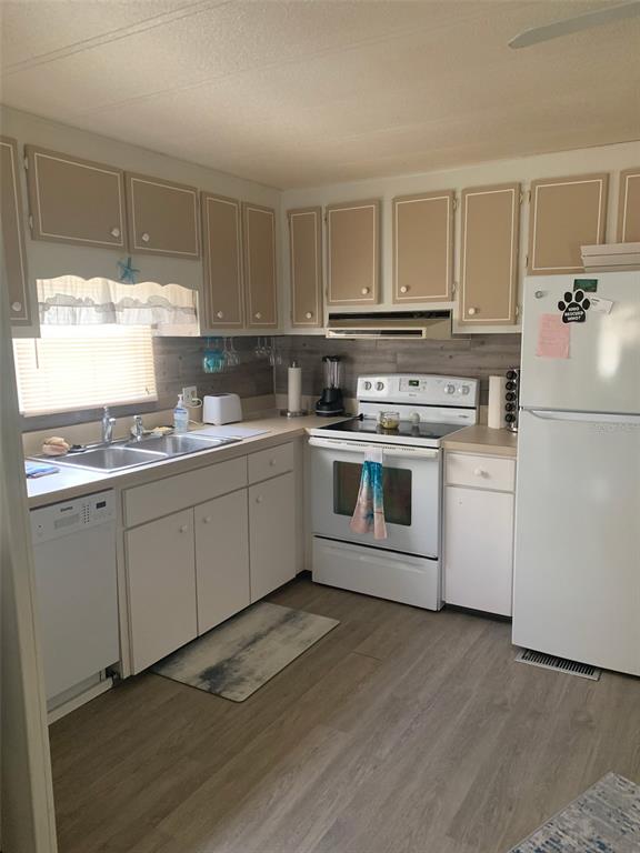 A kitchen features white lower cabinets, tan upper cabinets, white appliances, and wood-look flooring — 2341 BARON DRIVE, HOLIDAY, FL