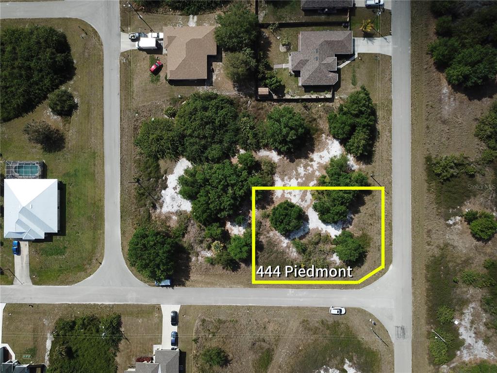 This is an aerial view of a vacant, wooded residential lot outlined in yellow — 444 PIEDMONT STREET, LEHIGH ACRES, FL
