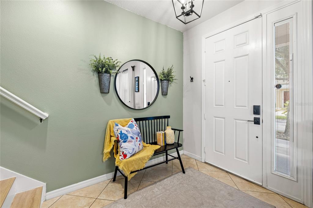 An entryway features a sage green wall, a black bench, a round mirror, and tile flooring — 7951 NORTHLAKE PARKWAY, ORLANDO, FL