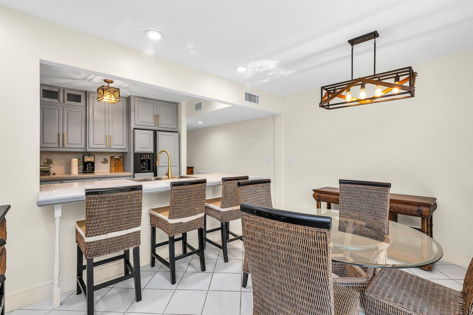 A kitchen with gray cabinets and a breakfast bar overlooks a dining area with wicker chairs — 584 SE 20th Avenue # 2, Deerfield Beach FL 33441, DEERFIELD BEACH, FL