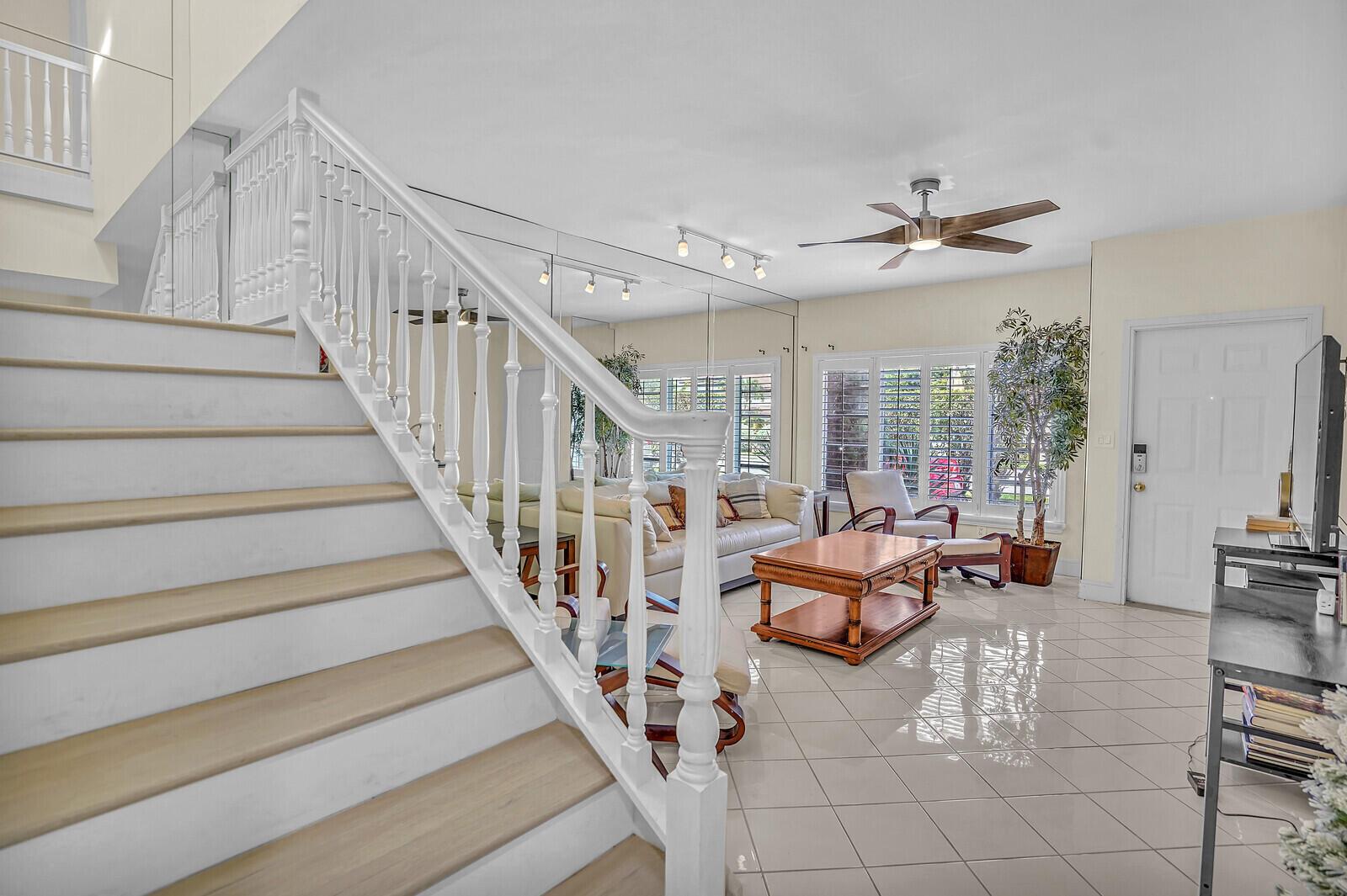 A living room with tiled floors, a wooden coffee table, and a staircase with white railings — 584 SE 20th Avenue # 2, Deerfield Beach FL 33441, DEERFIELD BEACH, FL