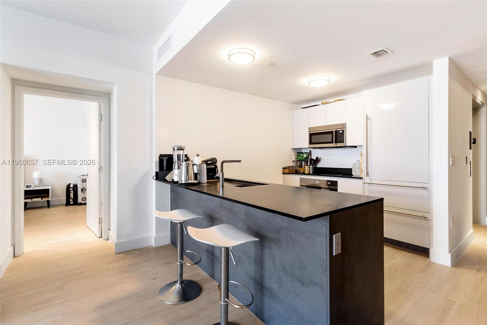 A modern kitchen features a dark gray island with bar stools and white cabinetry — 1010 Brickell Ave # 1404, Miami FL 33131, MIAMI, FL