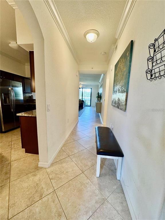 A tiled hallway features a dark bench, a wall painting, and an adjacent kitchen area — 16706 VARDON TERRACE UNIT 104, BRADENTON, FL