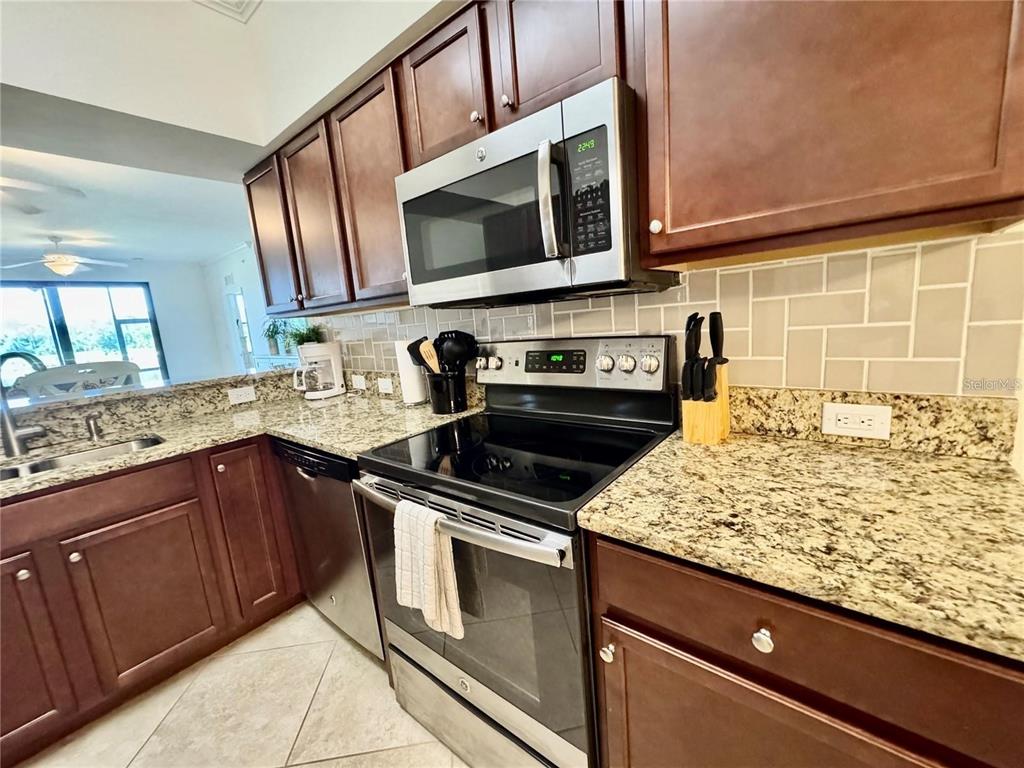A kitchen features dark wood cabinets, granite countertops, stainless steel appliances, and a tiled backsplash — 16706 VARDON TERRACE UNIT 104, BRADENTON, FL