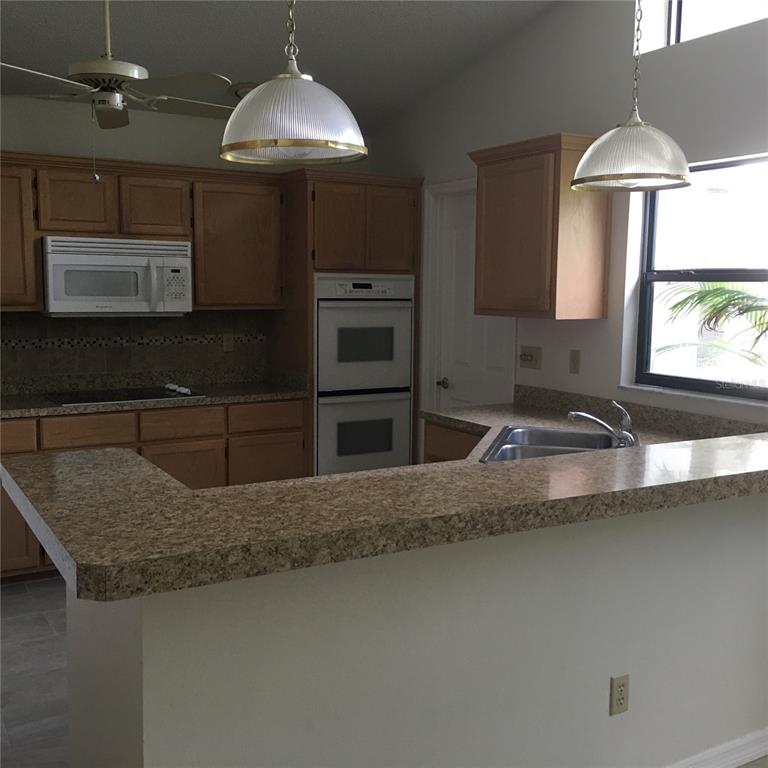 A kitchen features light wood cabinets, granite countertops, a double wall oven, and pendant lighting — 1912 FAYETTEVILLE AVENUE, DELTONA, FL