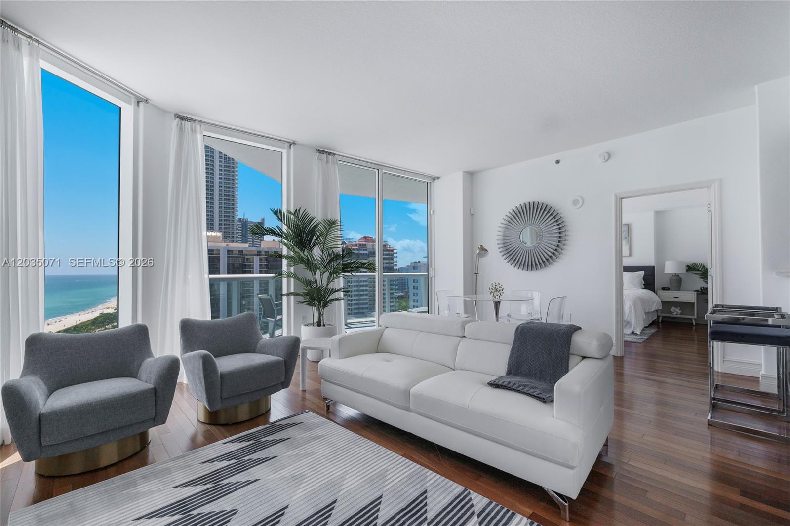 A modern living room features a white sofa, two gray armchairs, and floor-to-ceiling windows — 6515 Collins Ave # 1405, Miami Beach FL 33141, MIAMI BEACH, FL
