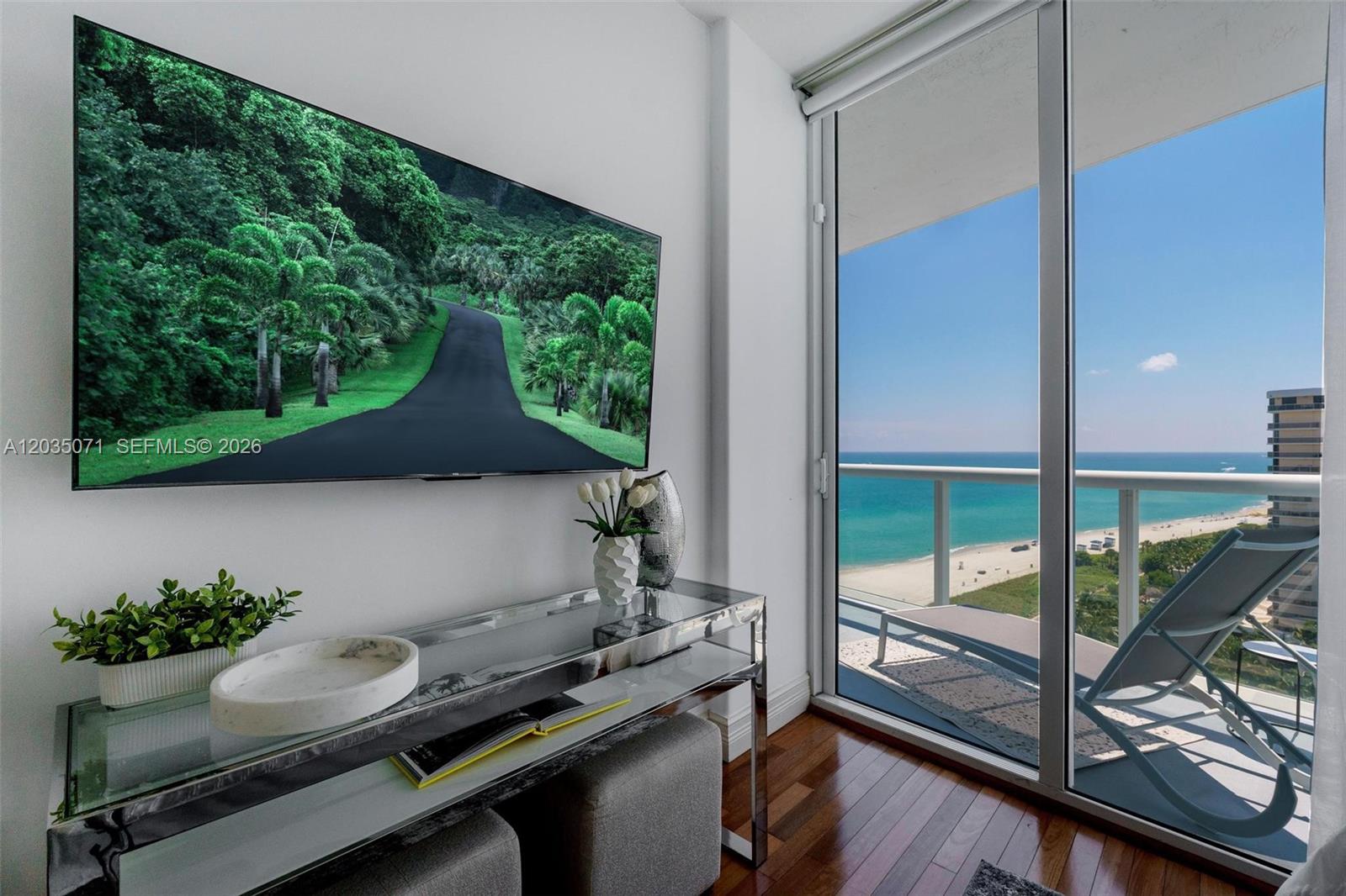 A living area features a wall-mounted television, a glass console table, and a balcony view — 6515 Collins Ave # 1405, Miami Beach FL 33141, MIAMI BEACH, FL