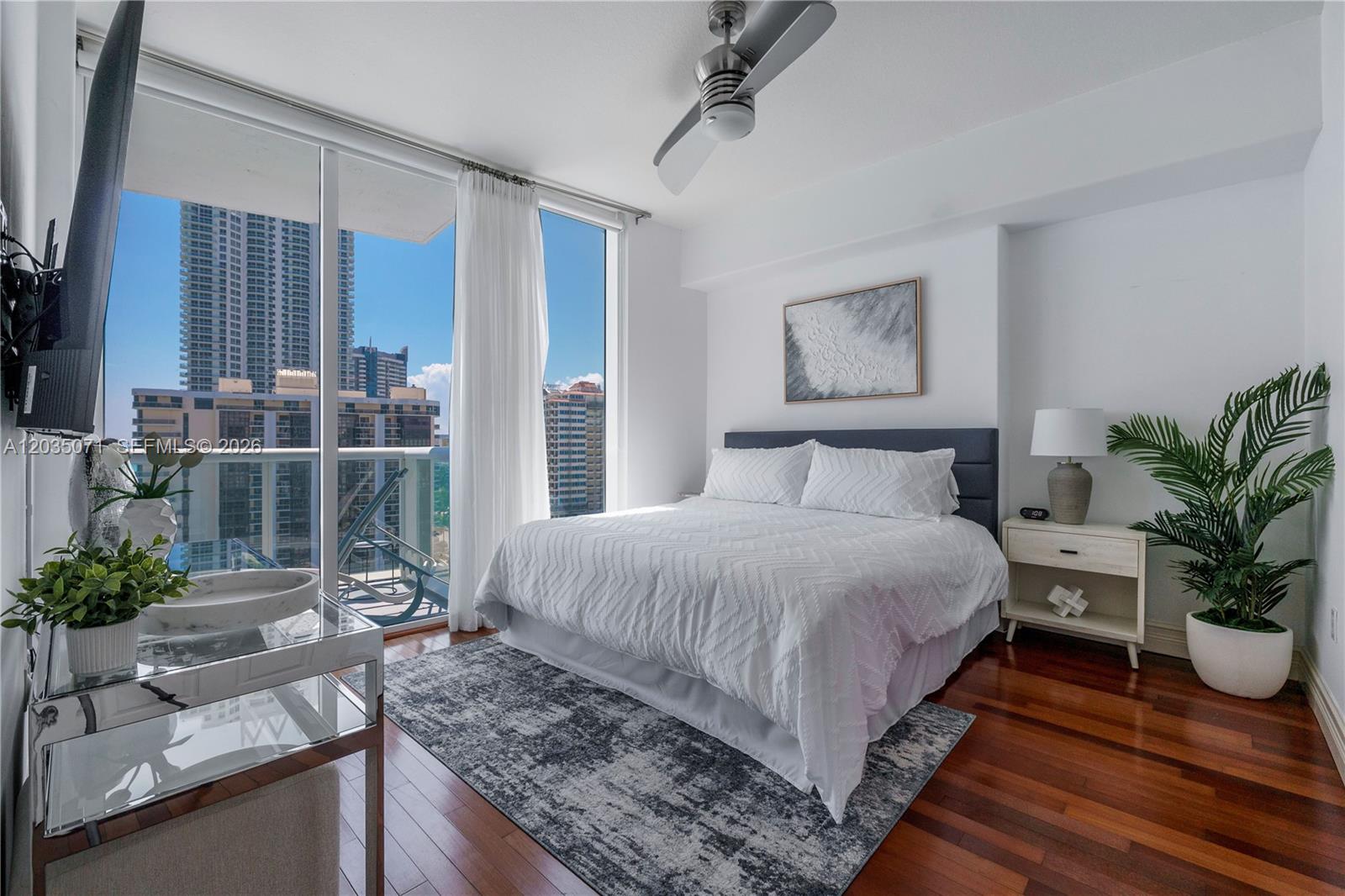 A bedroom features a bed, hardwood floors, a ceiling fan, and a balcony with city views — 6515 Collins Ave # 1405, Miami Beach FL 33141, MIAMI BEACH, FL