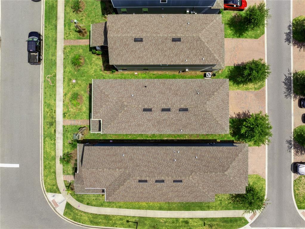 An aerial view shows three adjacent houses with brown shingled roofs and paved driveways — 12597 ENCORE AT OVATION WAY, WINTER GARDEN, FL