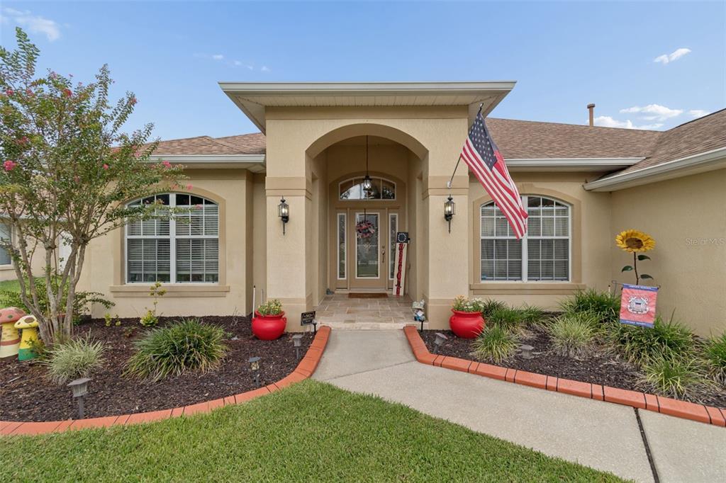 The exterior of a single-story stucco home features an arched entryway and an American flag — 3119 BLACKWATER OAKS WAY, MULBERRY, FL