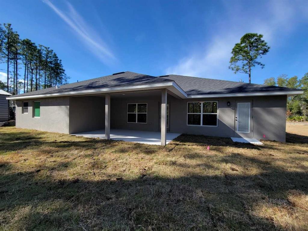 The rear exterior of a single-story gray house features a covered patio and lawn — 3121 SW 170TH PLACE, OCALA, FL