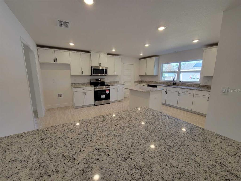 A modern kitchen features white cabinets, granite countertops, a center island, and stainless steel appliances — 3121 SW 170TH PLACE, OCALA, FL