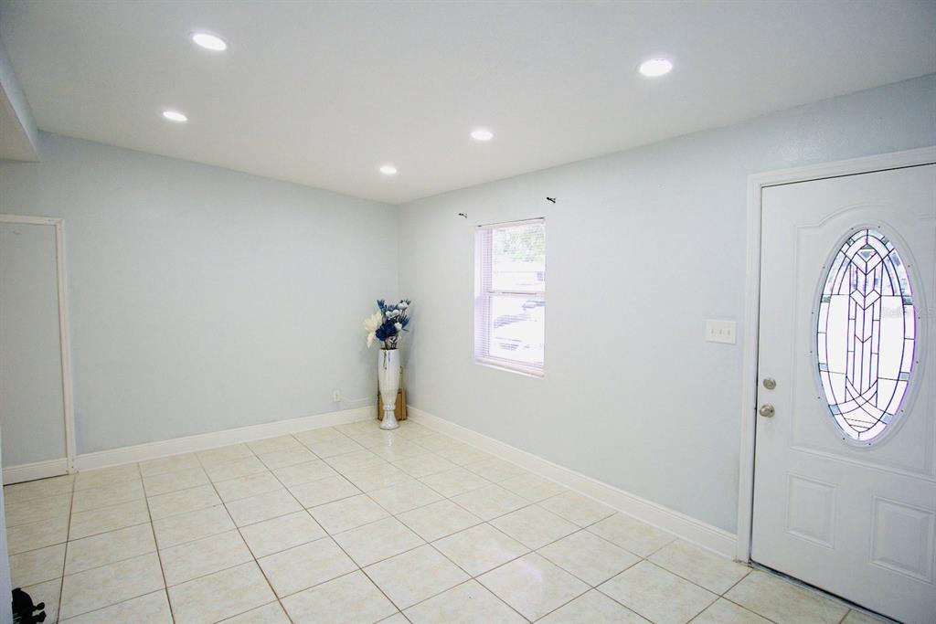 A bright room features light-colored tile flooring, white walls, recessed lighting, and a front door — 601 LIME TREE ROAD, TAMPA, FL
