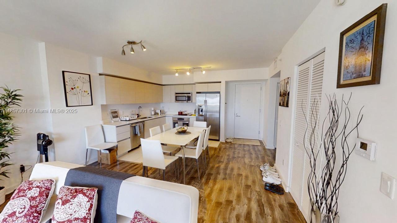 This open-concept kitchen and dining area features white cabinetry, stainless steel appliances, and wood flooring — 4250 Biscayne Blvd # 1008, Miami FL 33137, MIAMI, FL