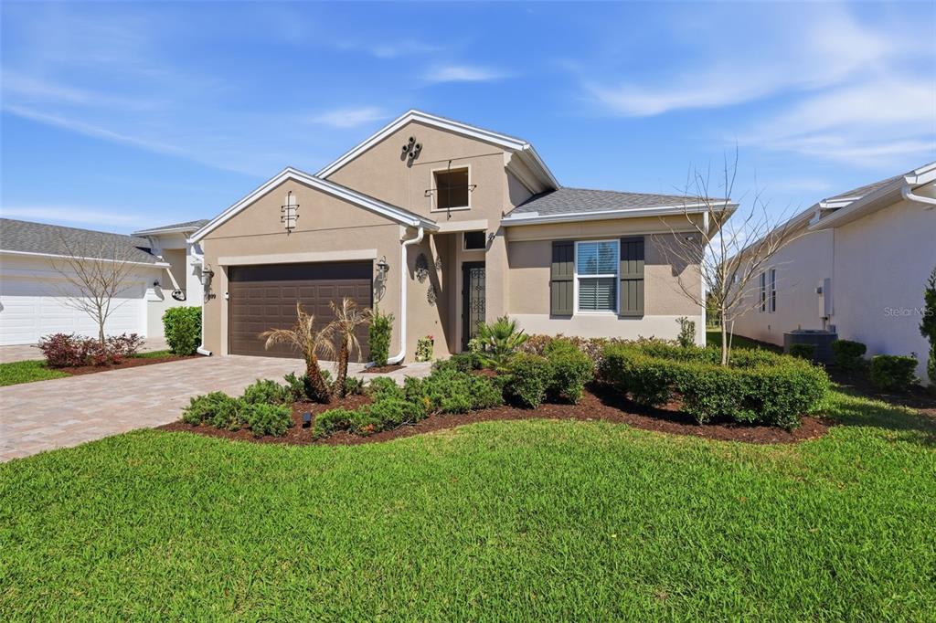 A single-story suburban house with a tan stucco exterior, brown garage door, and landscaped yard — 899 MEGANO BOULEVARD, DELAND, FL