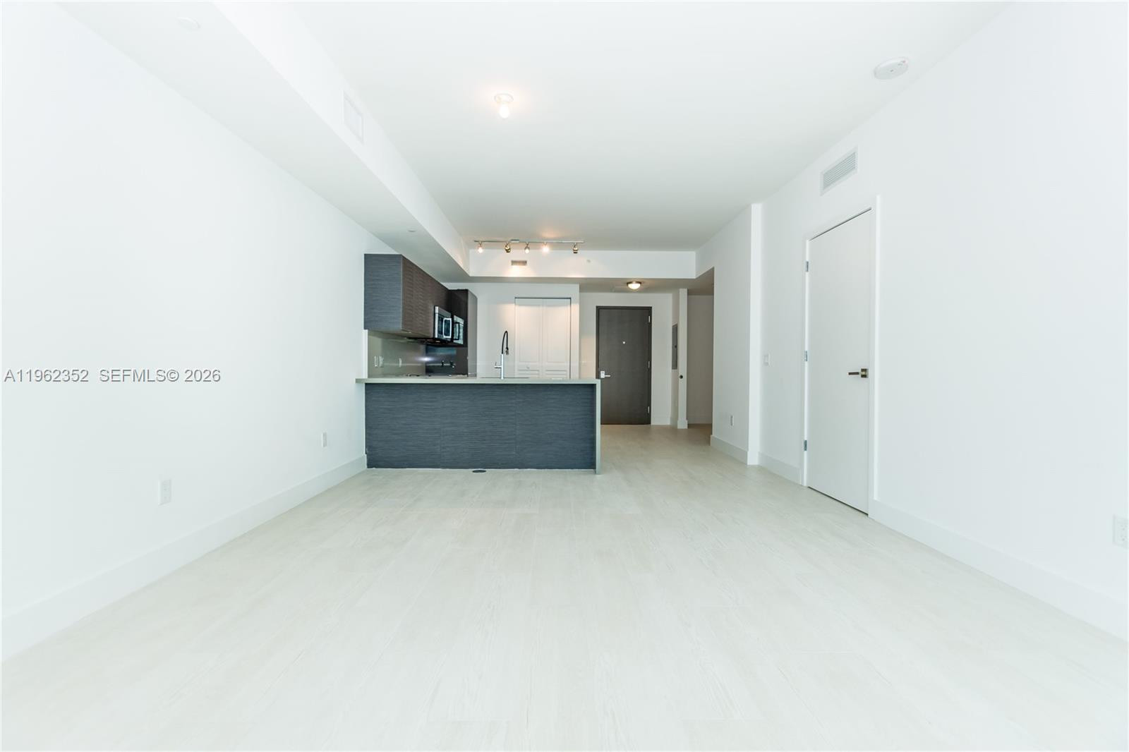 An open-concept living area features light wood-look flooring and a kitchen with dark cabinetry — 1080 Brickell Ave # 1706, Miami FL 33131, MIAMI, FL