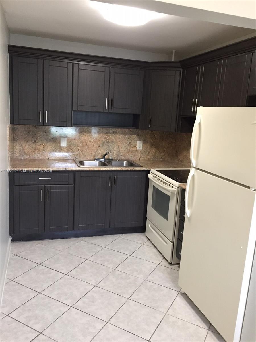 A kitchen features dark wood cabinets, granite countertops, a double sink, and white appliances — 182 Markham I # 182, Deerfield Beach FL 33442, DEERFIELD BEACH, FL