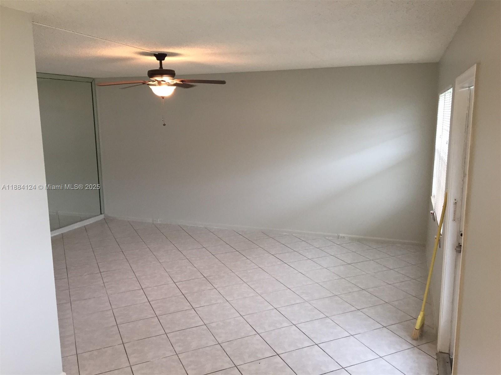 An empty room features light-colored tile flooring, a ceiling fan, and a glass sliding door — 182 Markham I # 182, Deerfield Beach FL 33442, DEERFIELD BEACH, FL