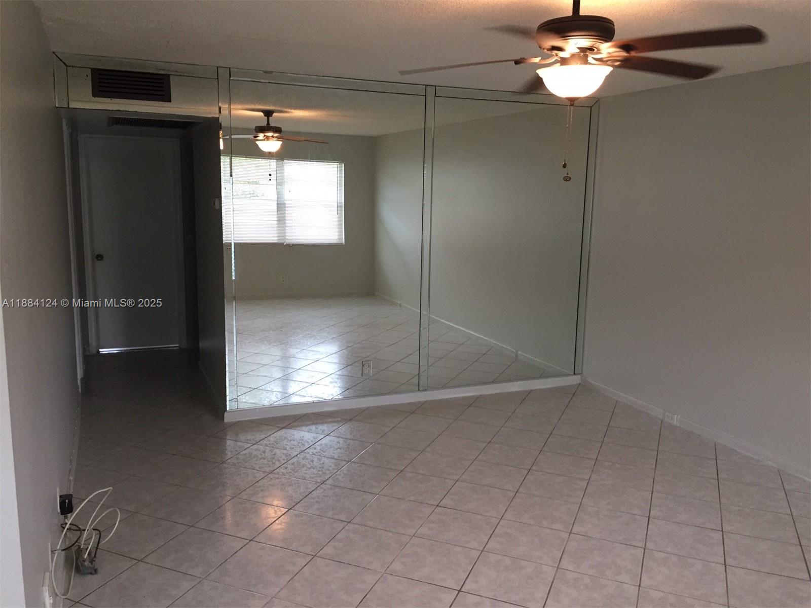 A room with tiled floors, a ceiling fan, and a large mirrored wall — 182 Markham I # 182, Deerfield Beach FL 33442, DEERFIELD BEACH, FL