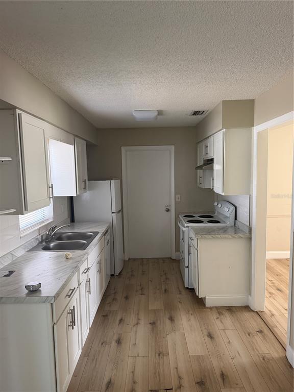 A galley-style kitchen features white cabinets, light wood-look flooring, and stainless steel appliances — 4518 GASPARILLA AVENUE, ORLANDO, FL
