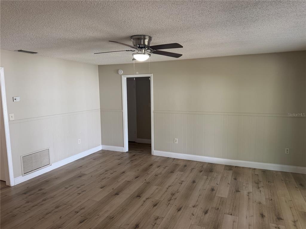 An empty room with wood-look flooring, beige walls with wainscoting, and a ceiling fan — 4518 GASPARILLA AVENUE, ORLANDO, FL