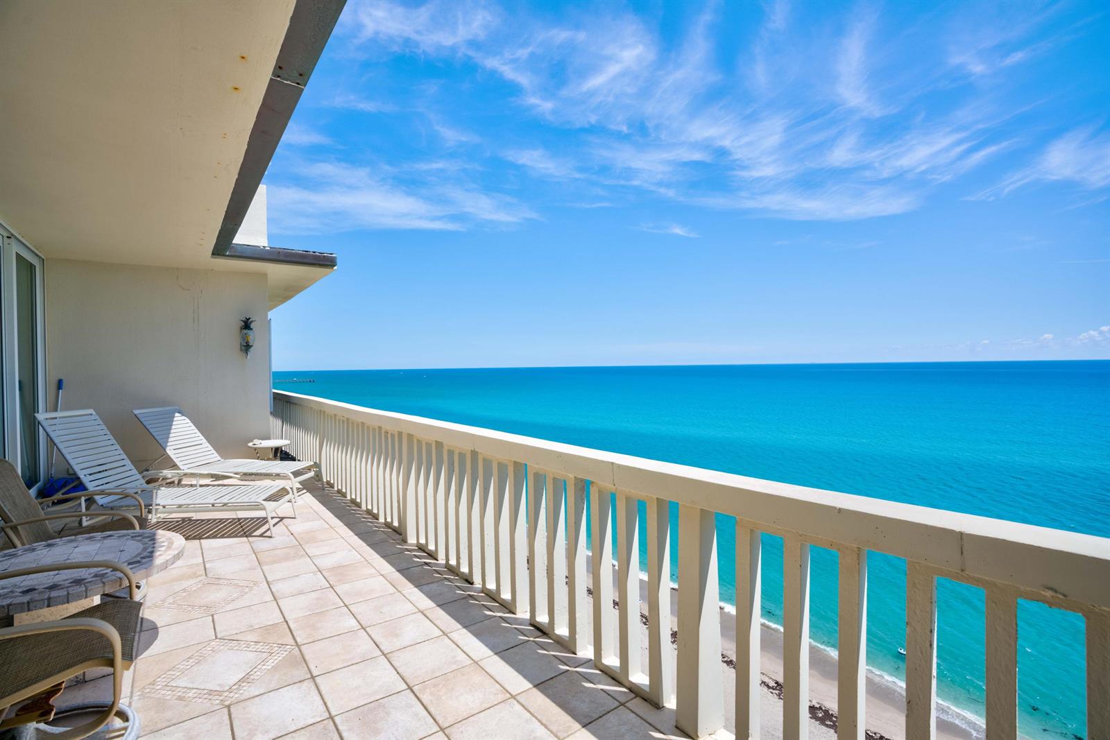 A tiled balcony with lounge chairs overlooks the ocean and a sandy beach below — 840 Ocean Drive # c, Juno Beach FL 33408, JUNO BEACH, FL