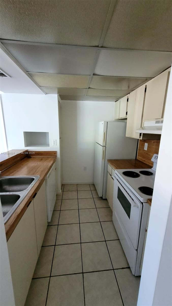 A galley kitchen features white cabinets, wood countertops, a white stove, and tile flooring — 6995 NW 186th St # E301, Hialeah FL 33015, HIALEAH, FL