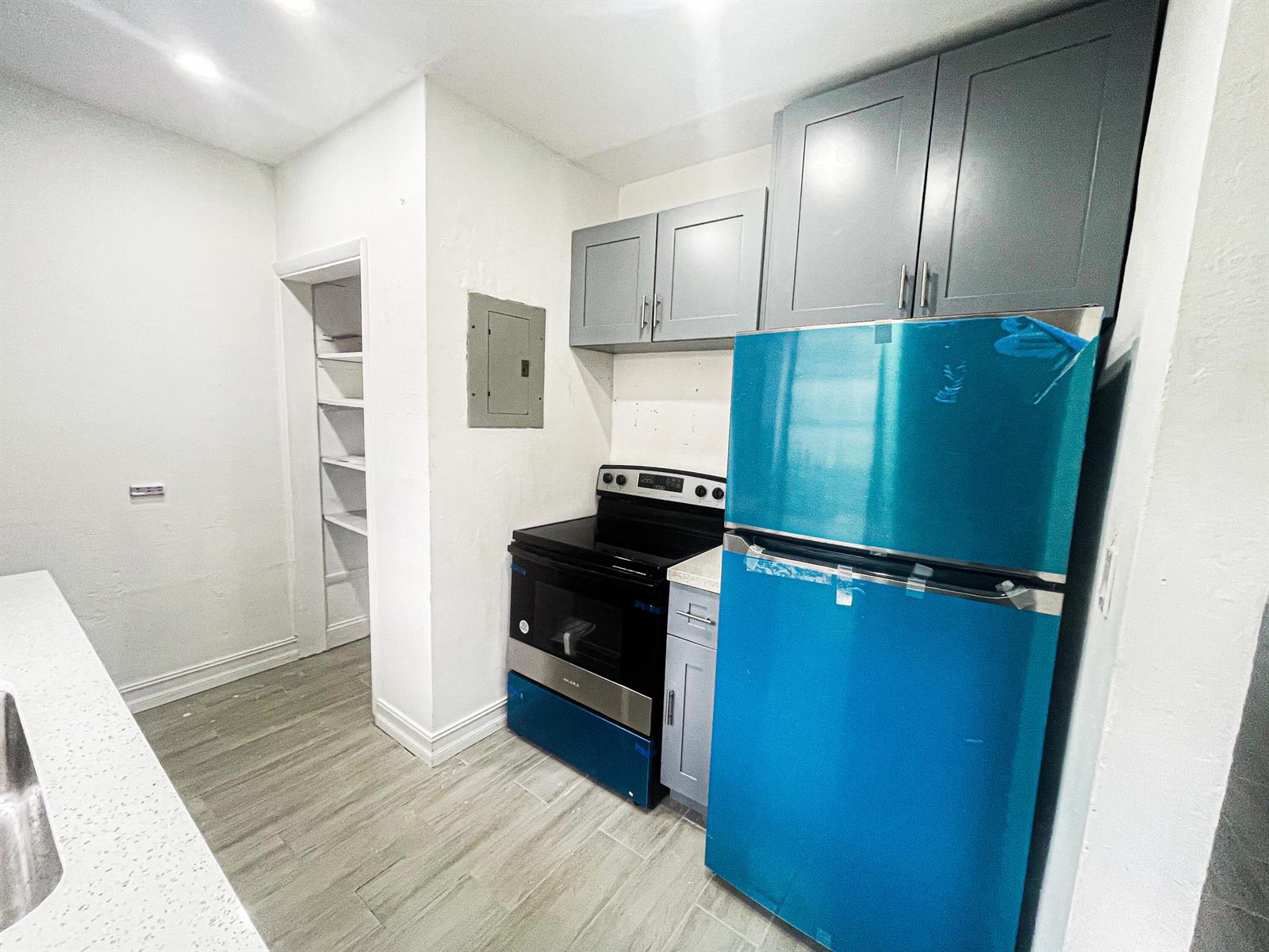 A kitchen features gray cabinets, a black stove, and a refrigerator with blue protective film — 841 NW 116th Terrace, Miami FL 33168, MIAMI, FL