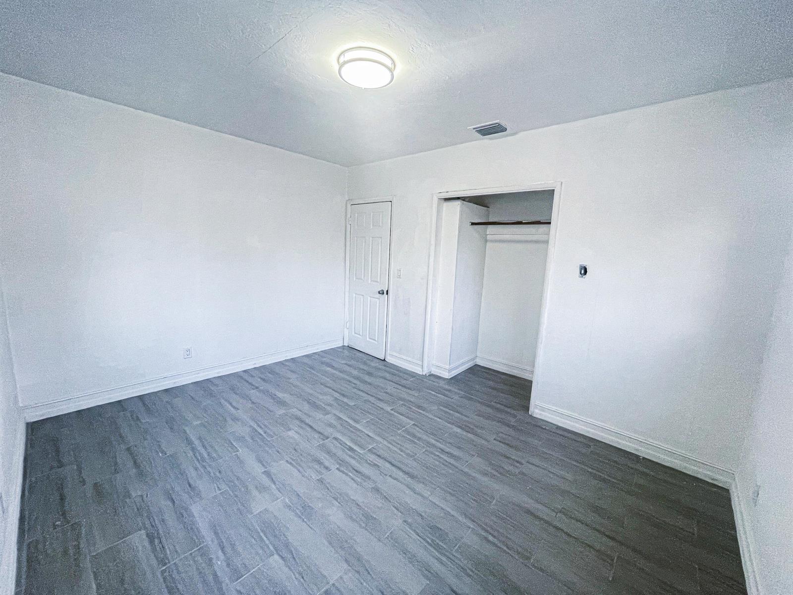 An empty bedroom features white walls, gray wood-look tile flooring, a closet, and a ceiling light — 841 NW 116th Terrace, Miami FL 33168, MIAMI, FL