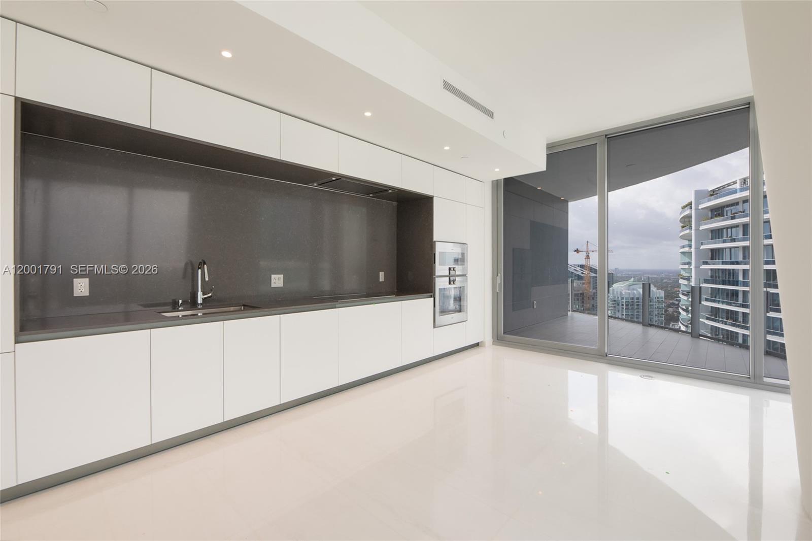A modern kitchen features white cabinetry, dark countertops, and floor-to-ceiling windows overlooking a city — 300 Biscayne Boulevard Way # 4708W, Miami FL 33131, MIAMI, FL